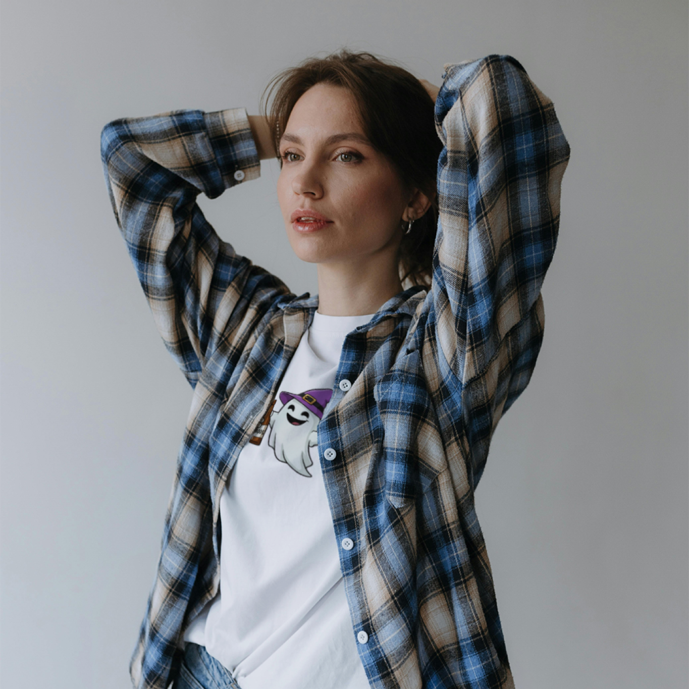 Person wearing a plaid shirt over a white t-shirt with a graphic design, standing against a plain background.