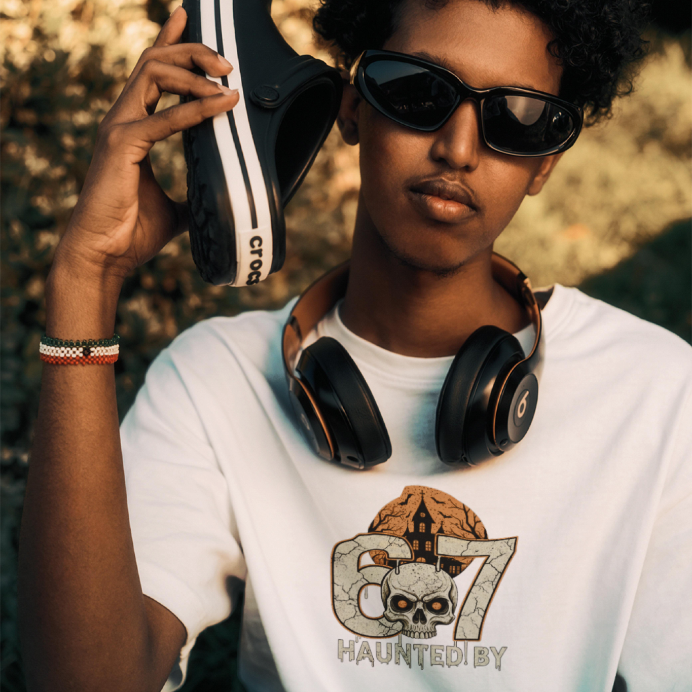Person wearing sunglasses and a white t-shirt with a graphic design, holding a black and white sneaker.