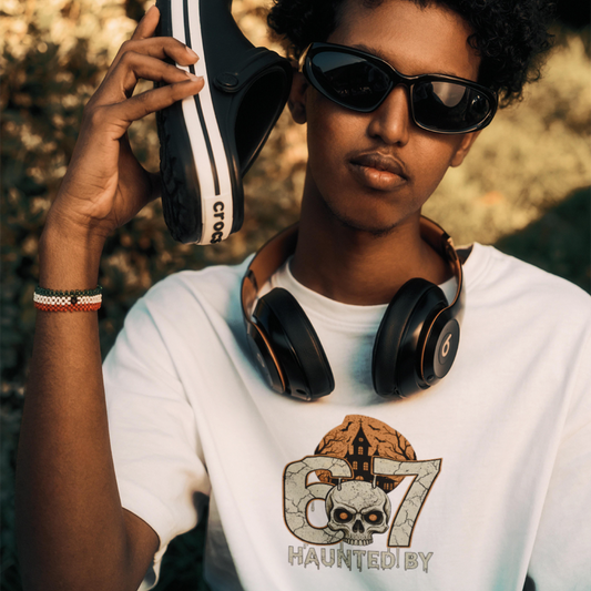 Person wearing sunglasses and a white t-shirt with a graphic design, holding a black and white sneaker.