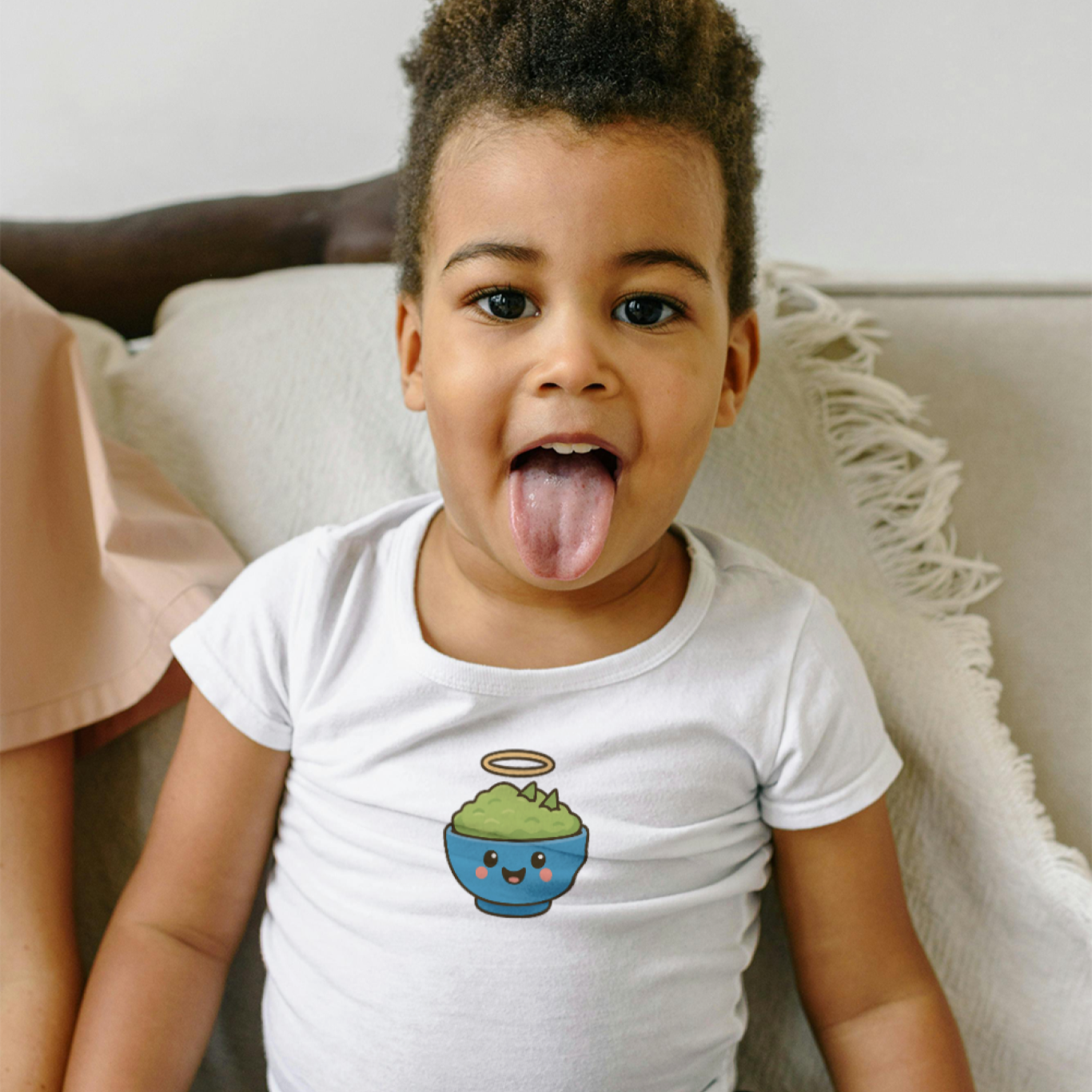Child wearing a white t-shirt with a graphic design, sitting on a couch.