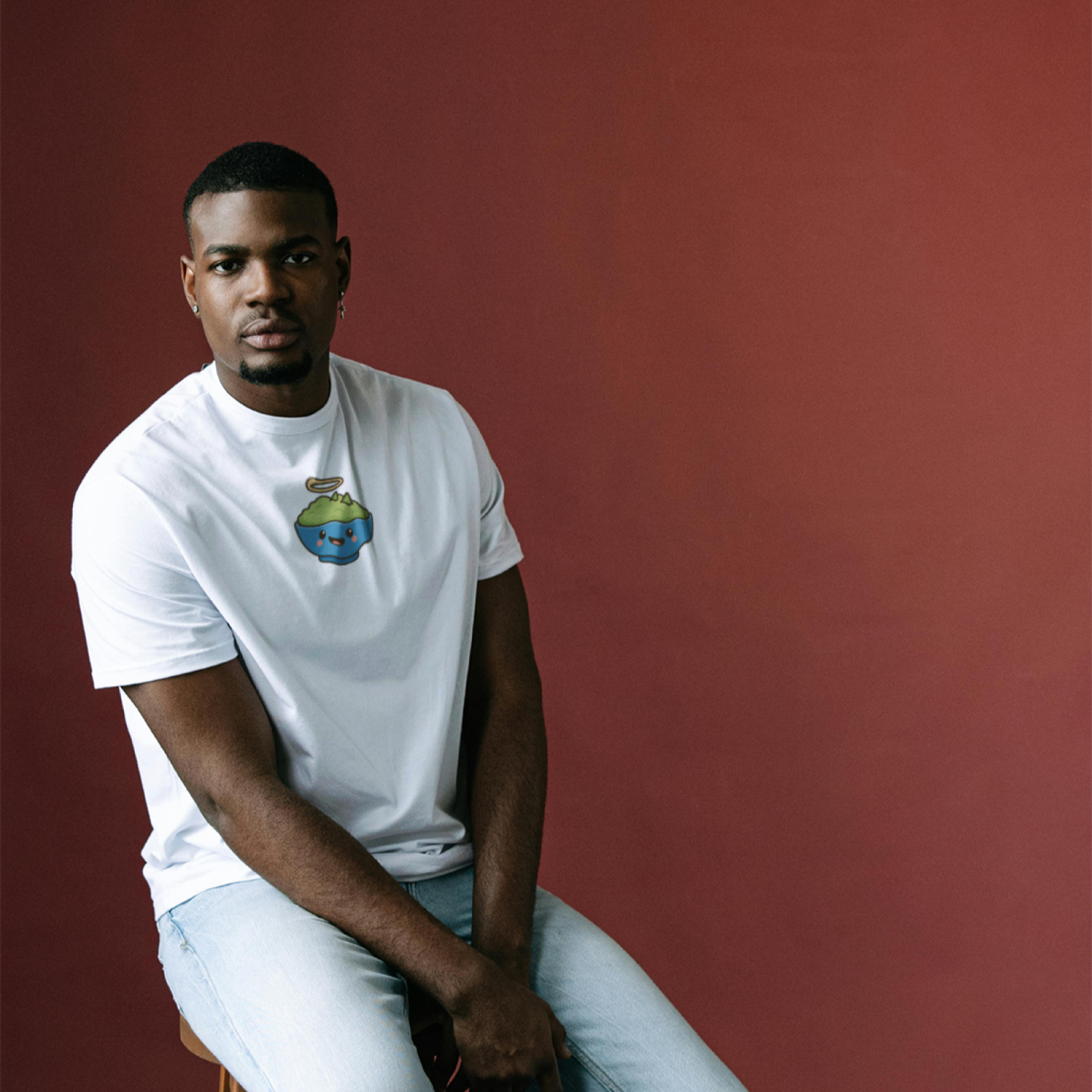 Man wearing a white t-shirt with a graphic design against a red curtain background