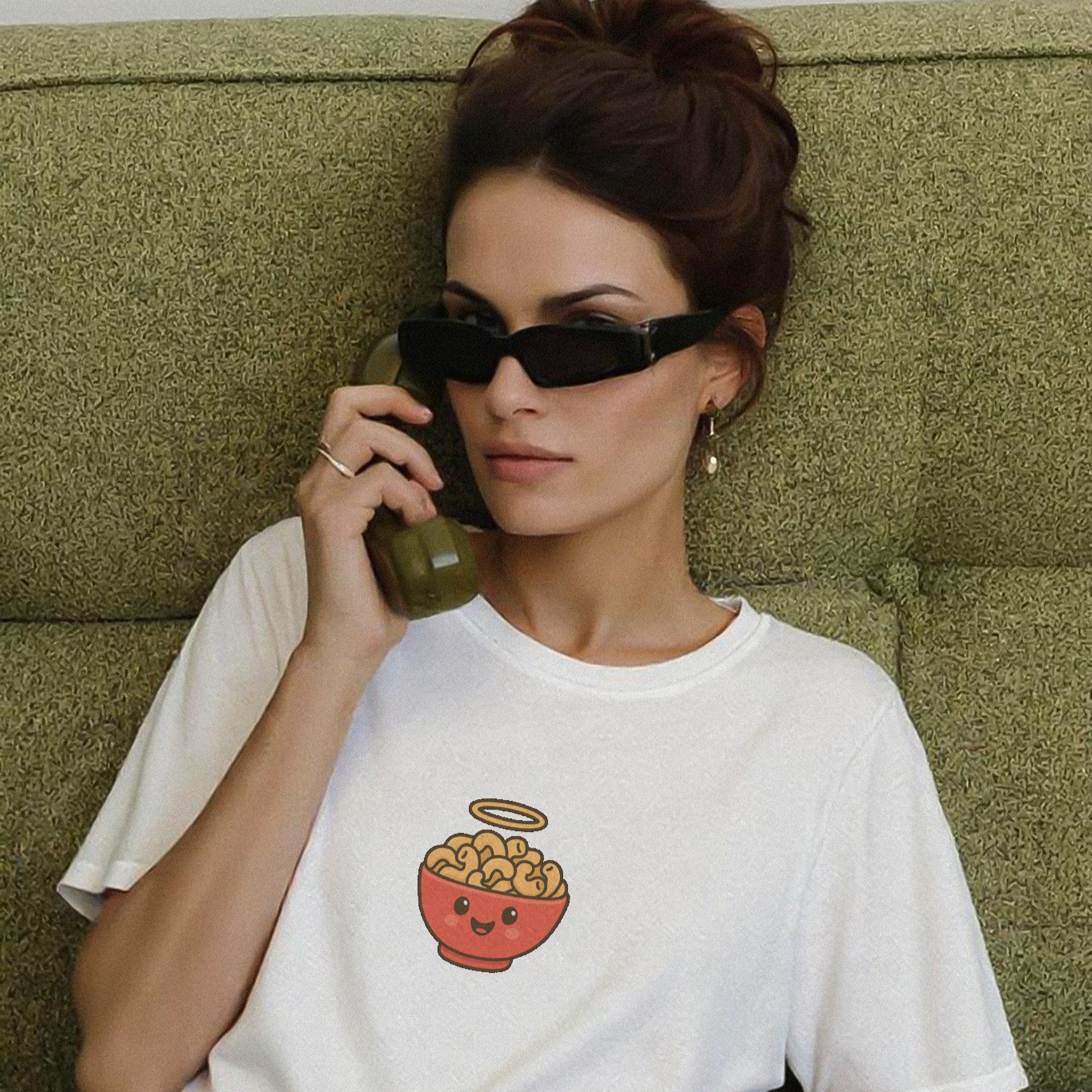 Woman wearing a white t-shirt with a graphic design, sitting on a green couch.