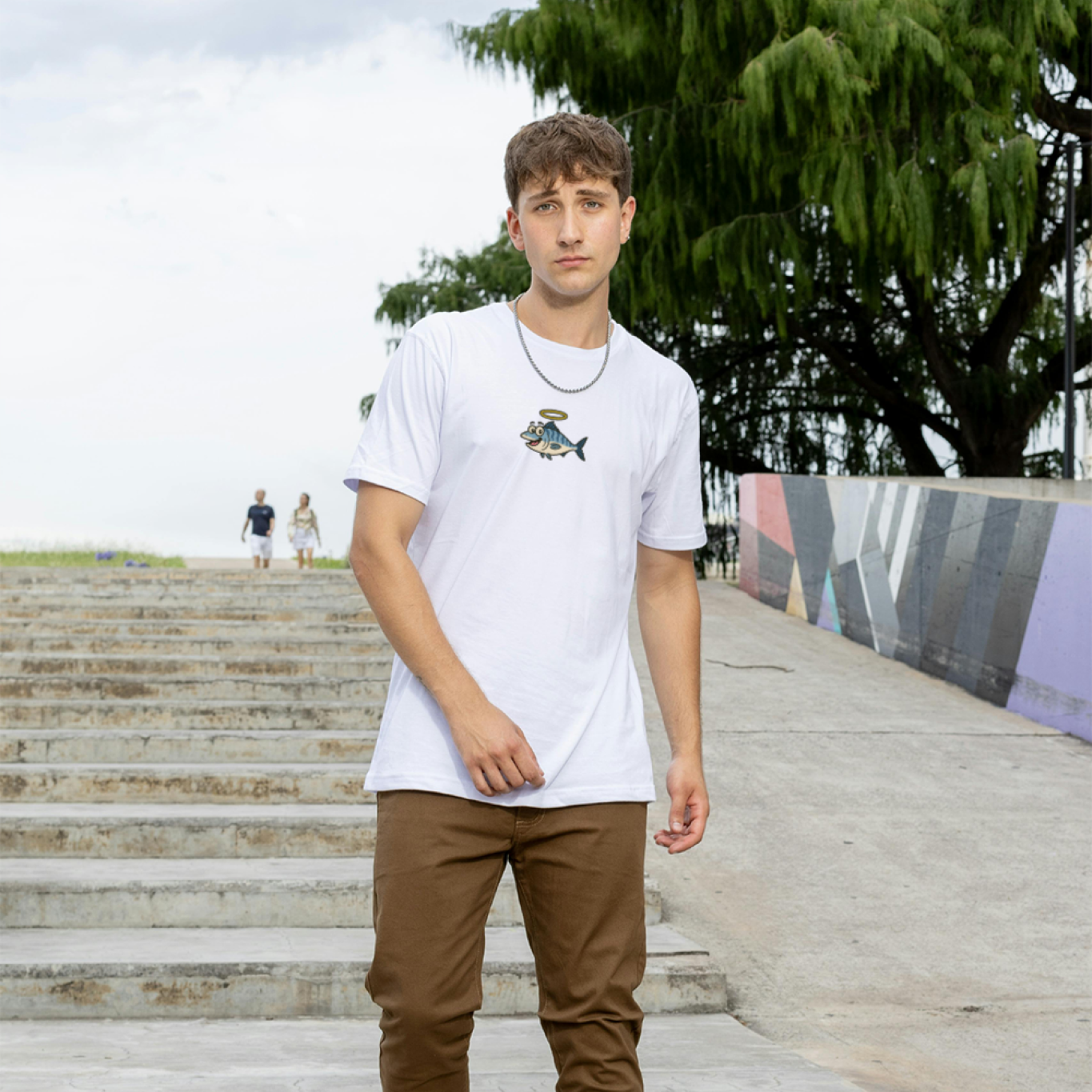 Man wearing a white t-shirt with a graphic design and brown pants standing on stone steps.