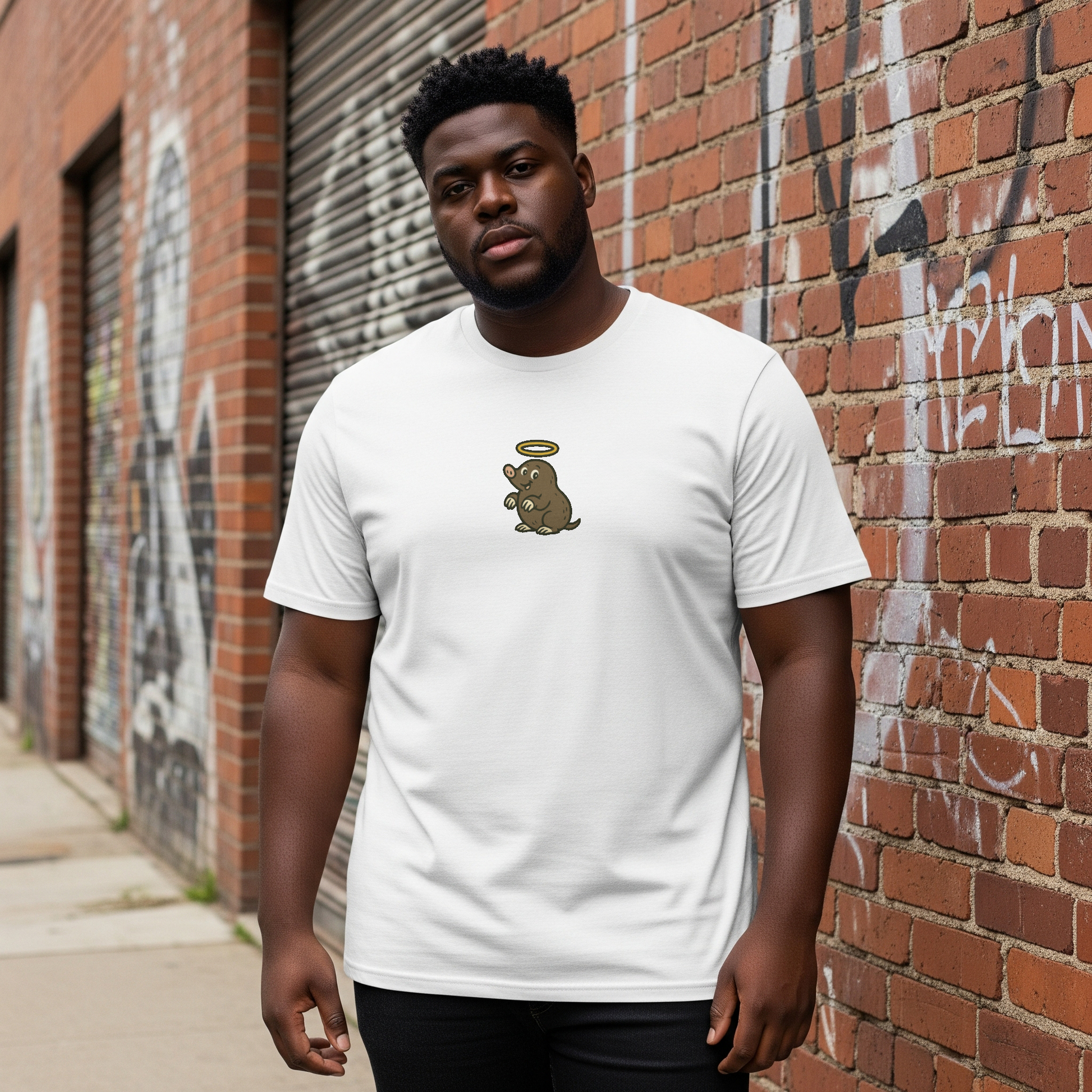 Man wearing a white t-shirt with a graphic design in front of a brick wall with graffiti.