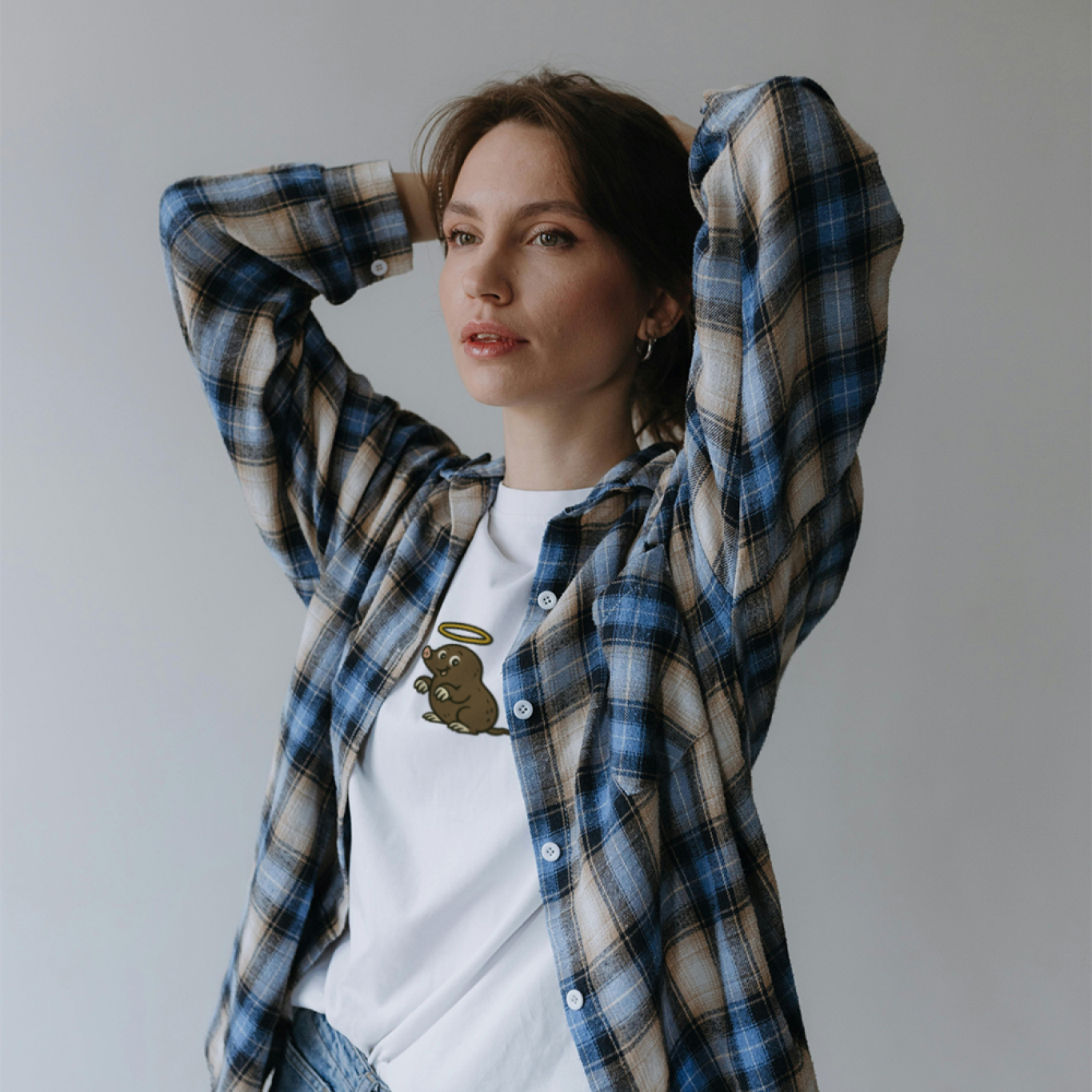 Woman wearing a plaid shirt over a white t-shirt with a graphic design, standing against a plain background.