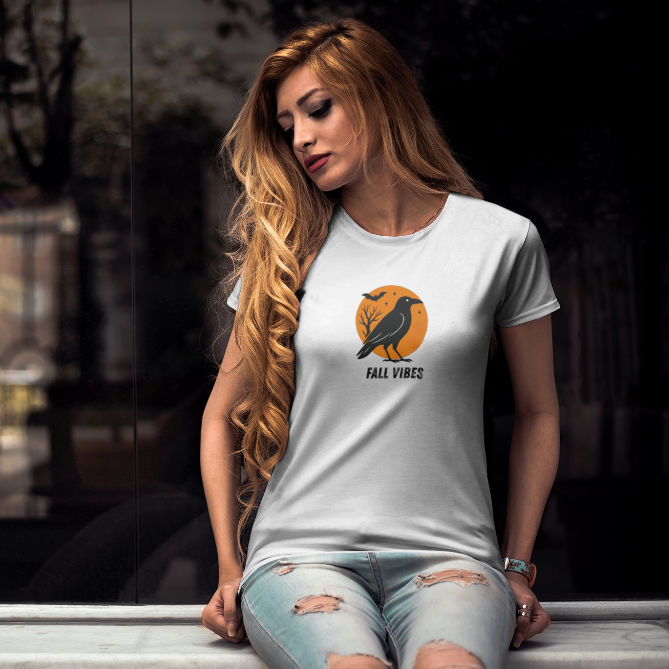 Woman wearing a white t-shirt with a graphic design sitting on a ledge.