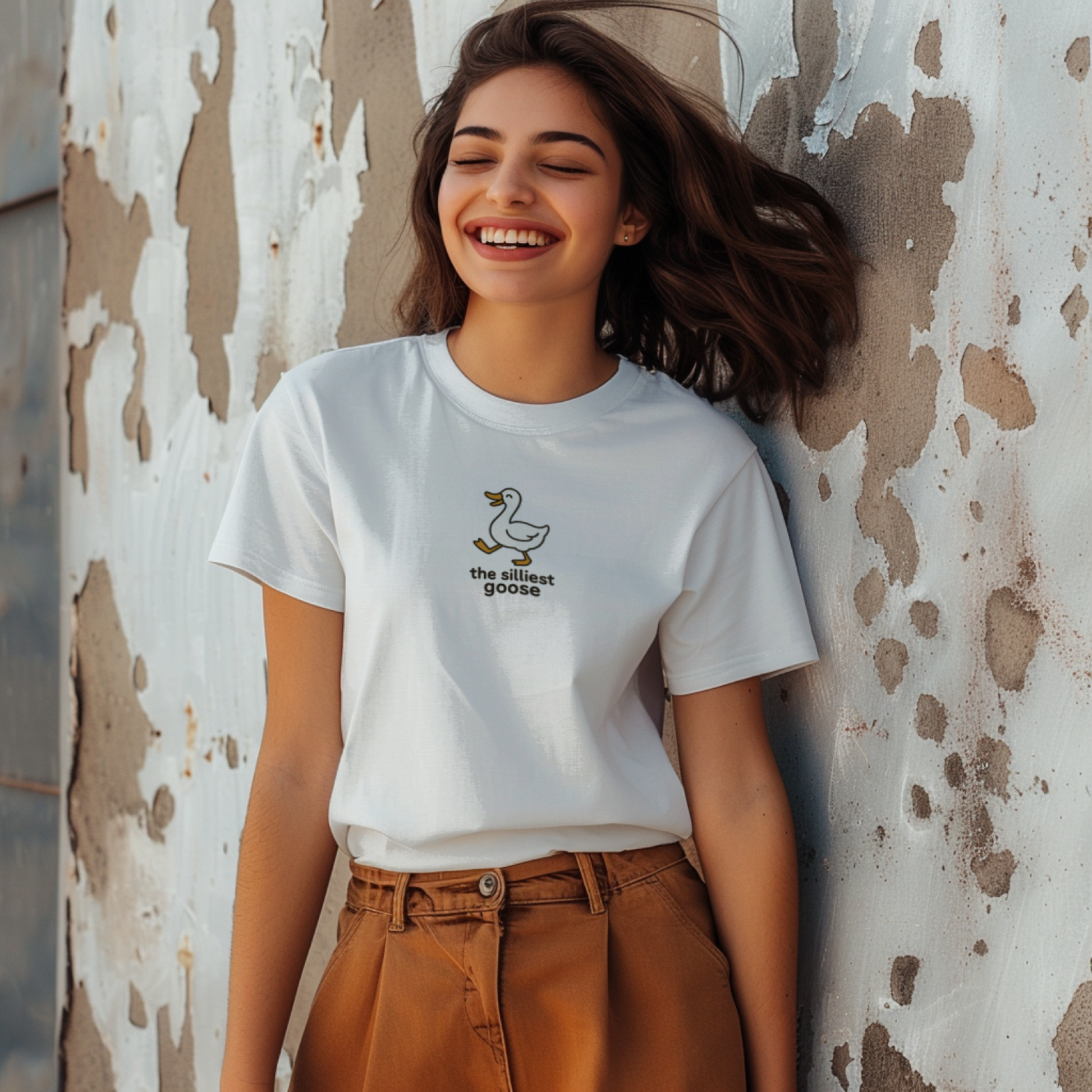 Woman wearing a white t-shirt with a logo against a textured wall.