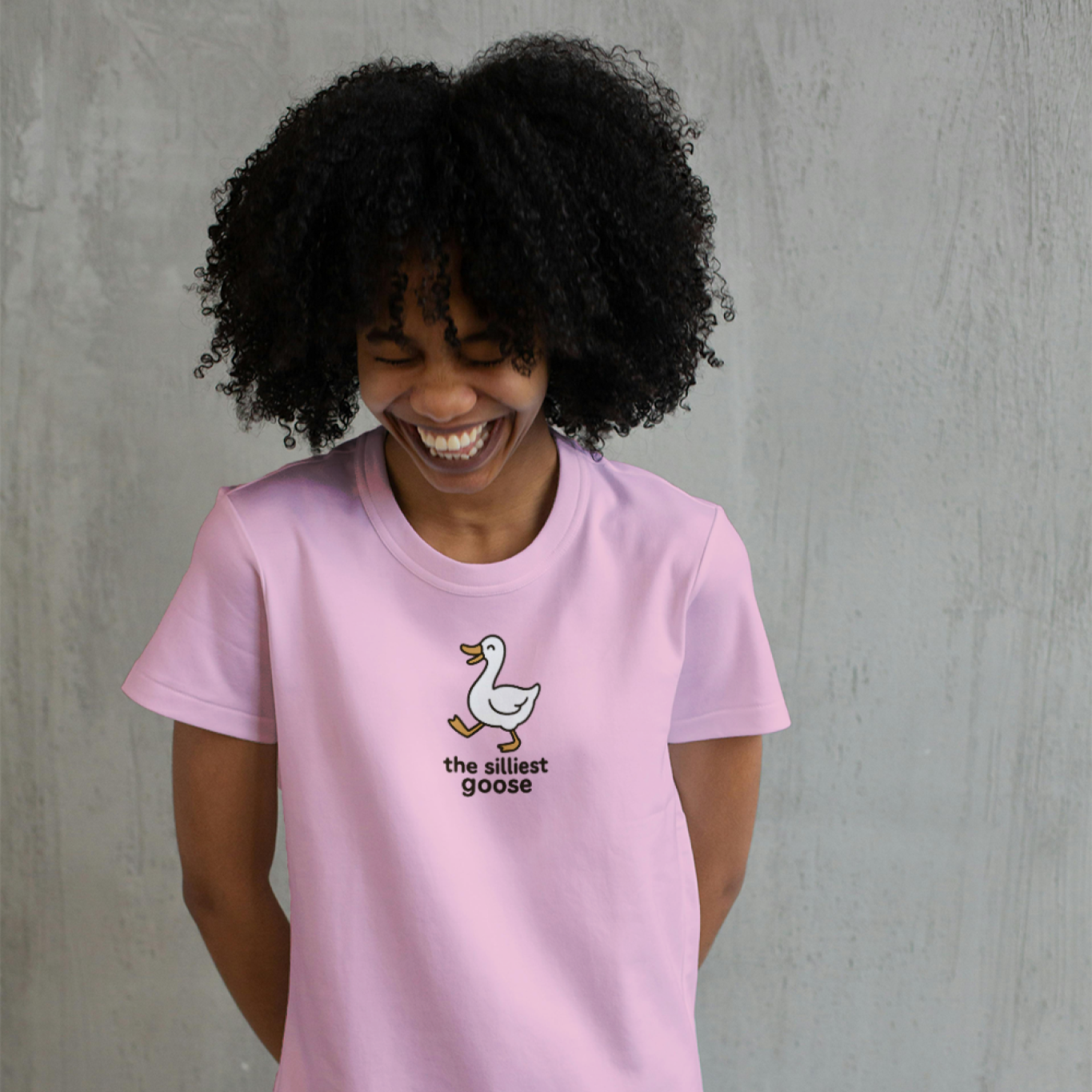 Person wearing a pink t-shirt with a duck graphic and text, standing against a gray background