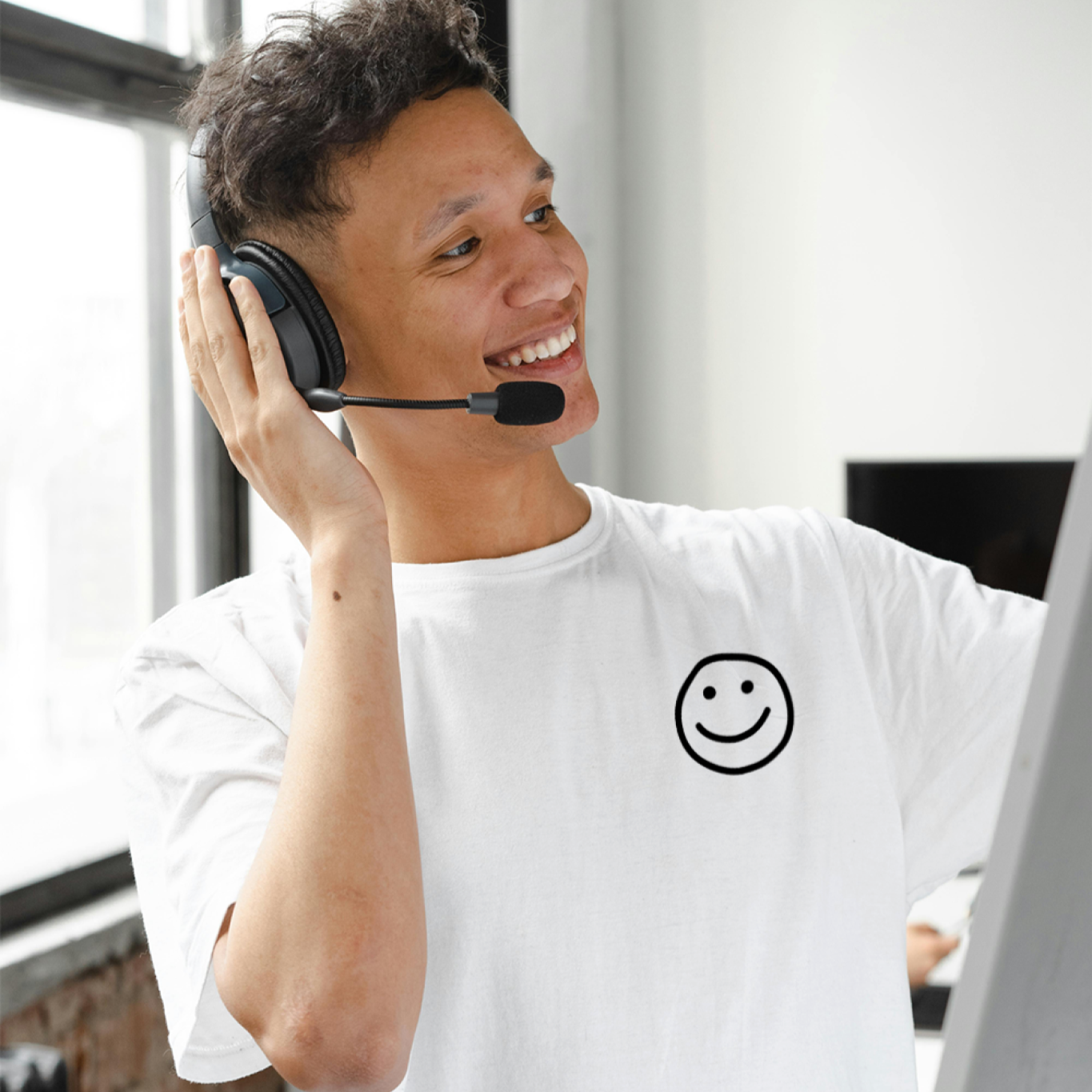 Person wearing a headset and smiling, sitting in front of a computer in an office setting.