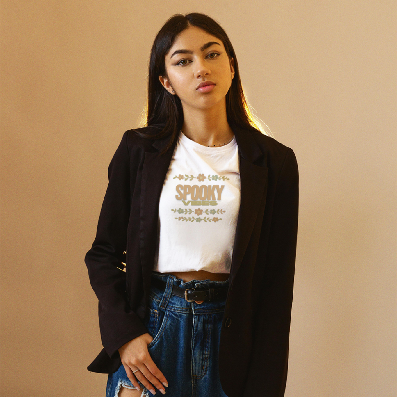 Person wearing a black blazer, white t-shirt with text, and ripped jeans on a beige background