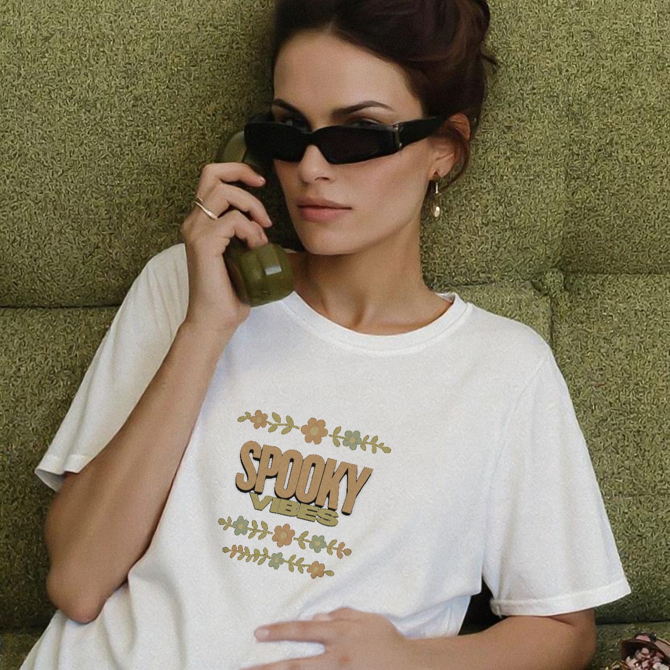 Woman wearing a white t-shirt with 'SPOOKY' text, sitting on a green couch.