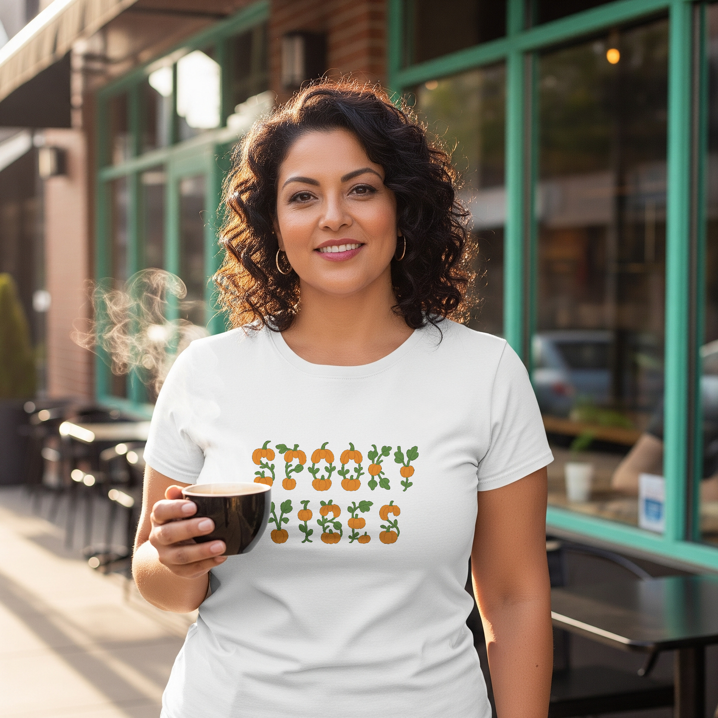 Woman holding a coffee cup wearing a white t-shirt with a graphic design in an urban setting.