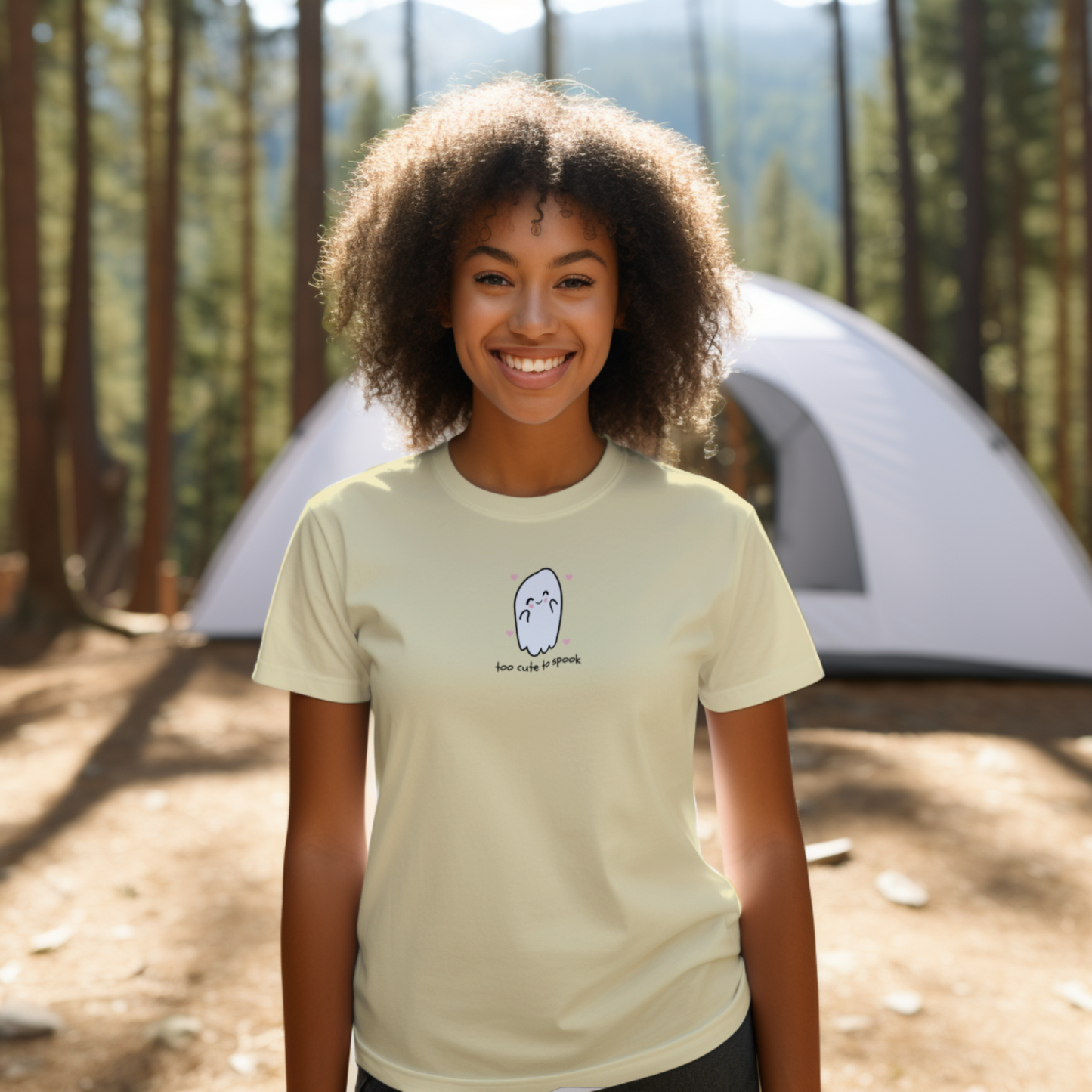 Person wearing a beige t-shirt with a graphic design in front of a tent in a forest setting