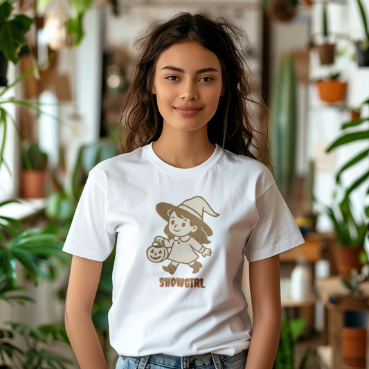 Woman wearing a white t-shirt with a graphic design of a showgirl holding a pumpkin, standing in a room with plants.
