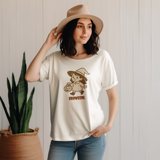 Woman wearing a white t-shirt with a graphic design and a beige hat, standing against a light wooden panel background.