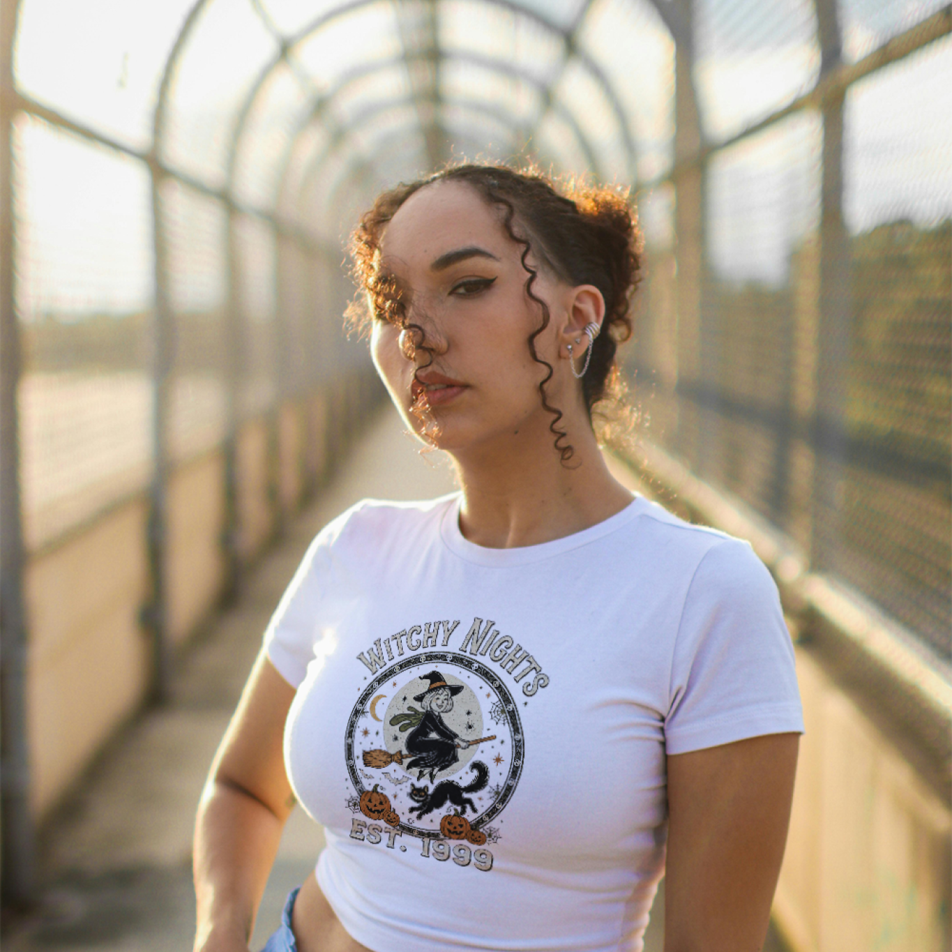 Person wearing a white t-shirt with a graphic design and light blue jeans on a bridge.