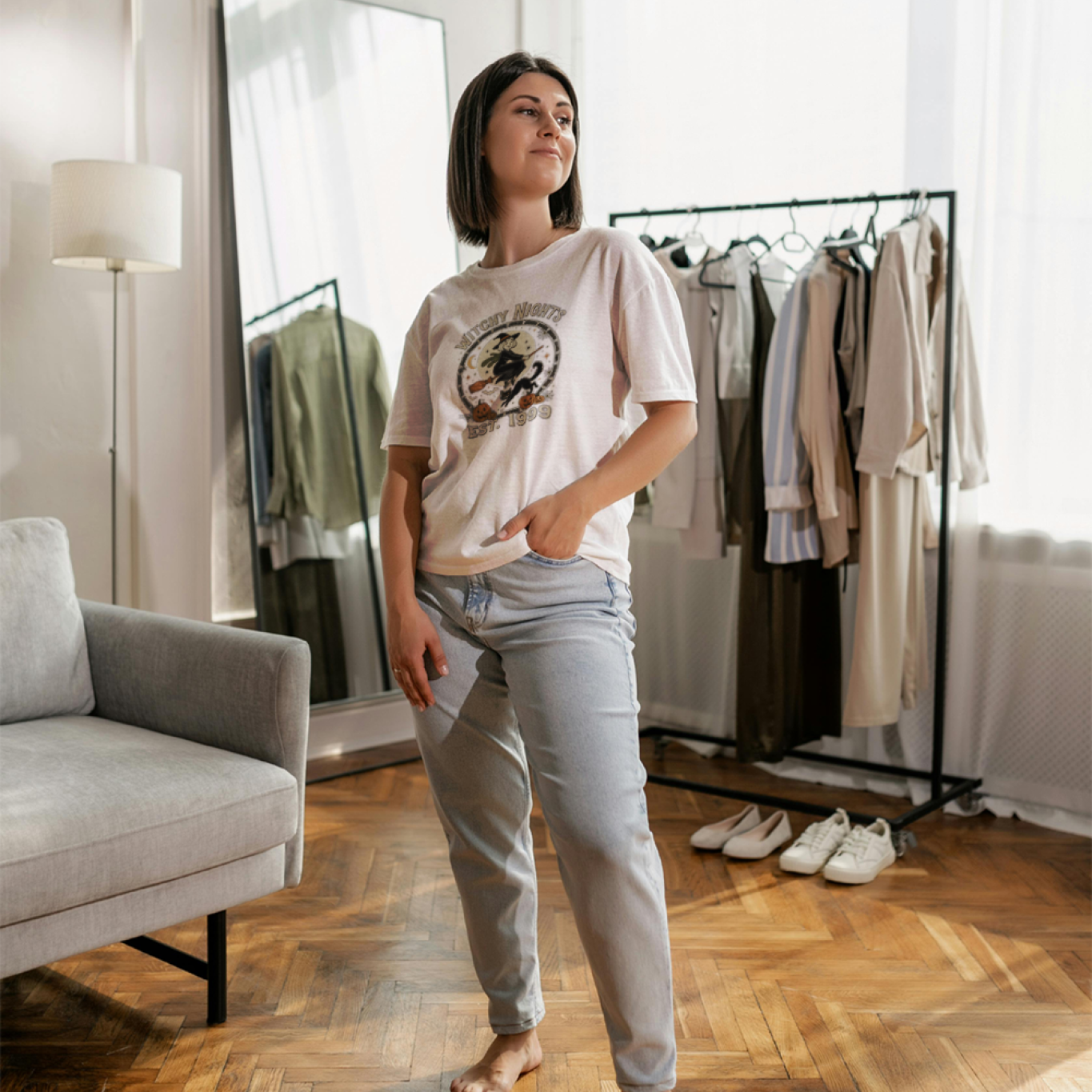 Woman standing in a room with clothes on racks and a mirror.