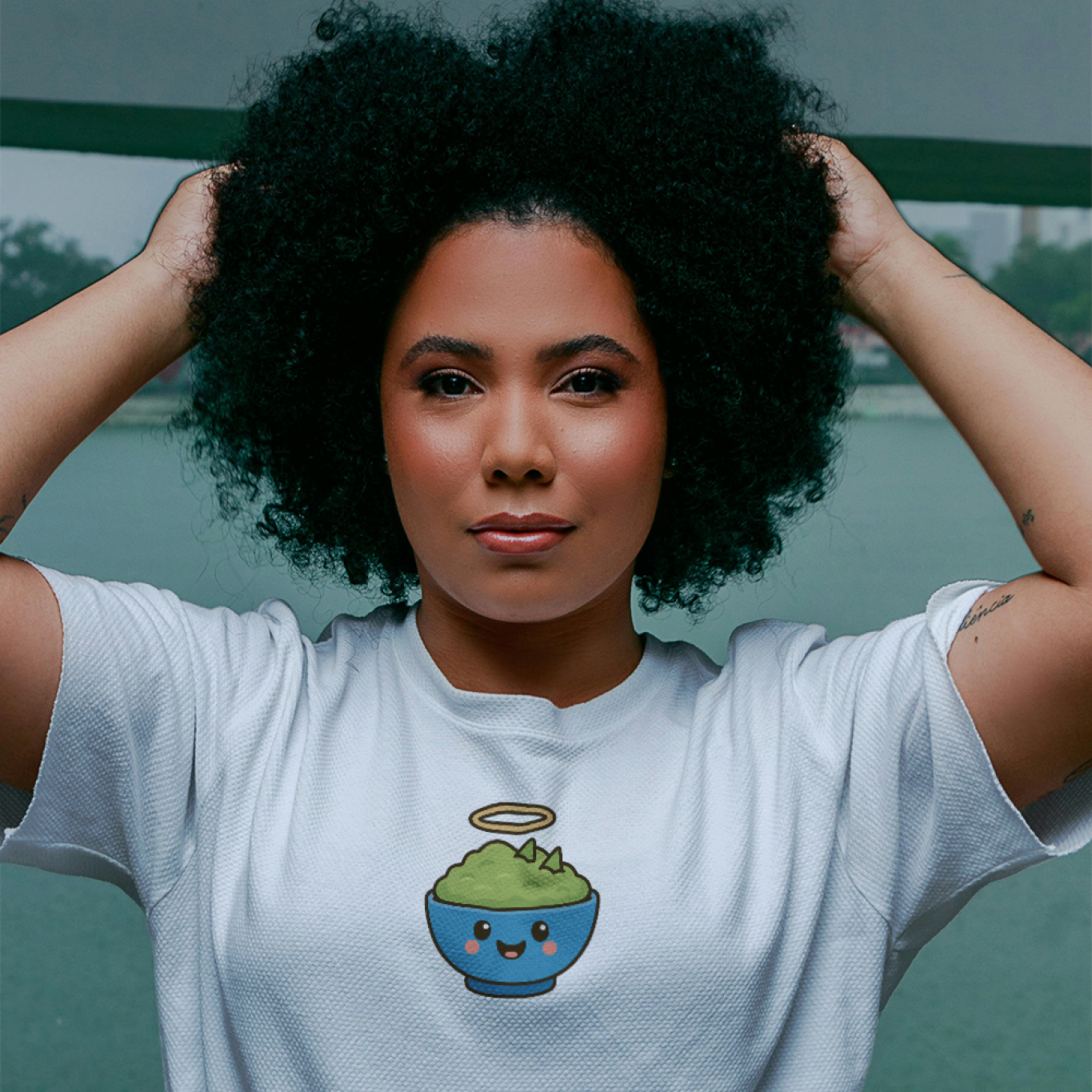Woman wearing a white t-shirt with a blue character design, standing against a blurred outdoor background.